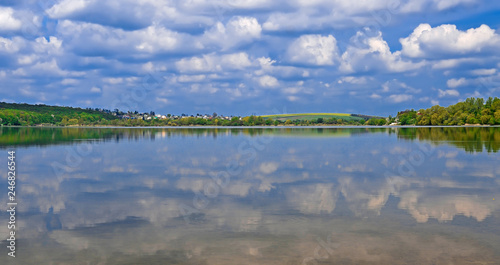 The island among the lake on which grow tall green trees against a blue sky with clouds
