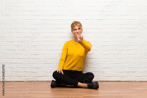 Young girl sitting on the floor smiling and showing victory sign