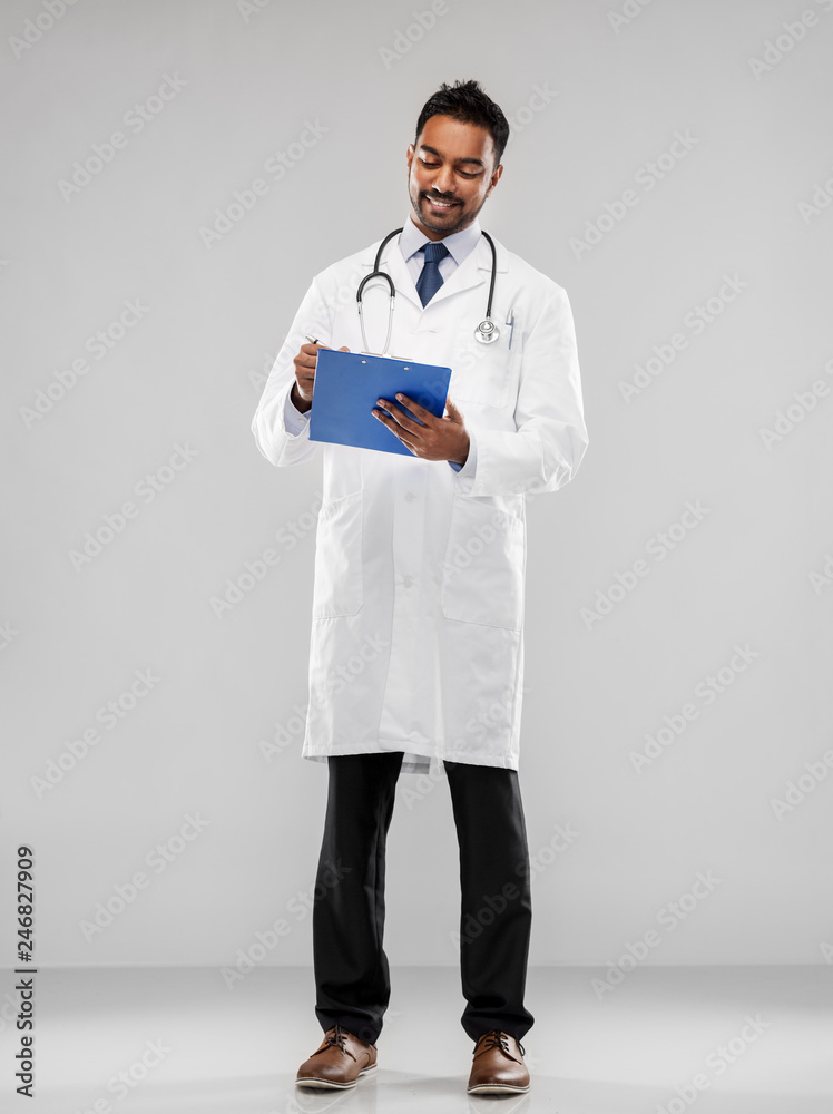 medicine, profession and healthcare concept - smiling indian male doctor in white coat with stethoscope and clipboard over grey background medicine, profession and healthcare concept - smiling indian male doctor in white coat with stethoscope and clipboard over grey background