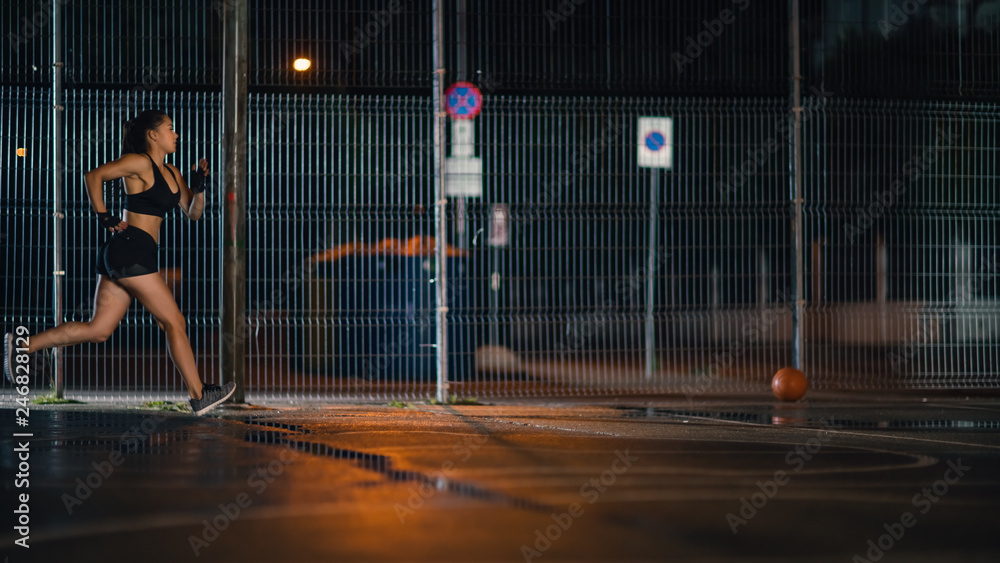 Beautiful Energetic Fitness Girl is Sprinting in a Fenced Outdoor Basketball Court. She's Running at Night After Rain in a Residential Neighborhood Area.