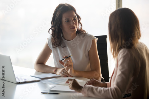 Fototapeta Two diverse serious businesswomen discussing business project working together i