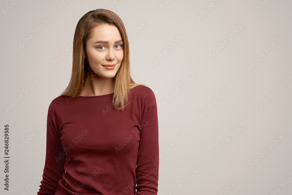 Photo of satisfied adorable young woman, smiles pleasantly at camera, rejoices coming holidays, isolated over white concrete wall. Positive human emotions