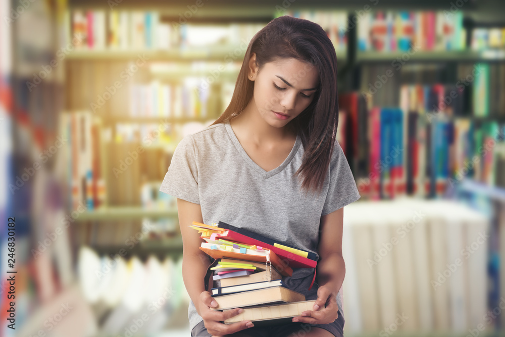 Young student woman serious and headache.work hard,study difficut. Many book put on leg.library background. Young student woman serious and headache.work hard,study difficut. Many book put on leg.library background.