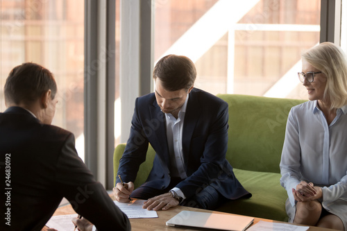 Two partners fill document form sign two-sided contracts for services at meeting, confident businessmen making sale purchase agreement deal put written signature on legal business papers