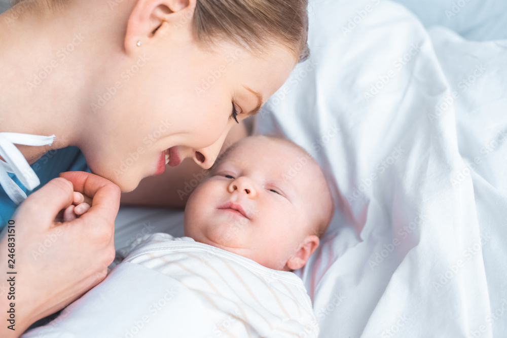 happy young mother holding hand of adorable newborn baby lying on bed