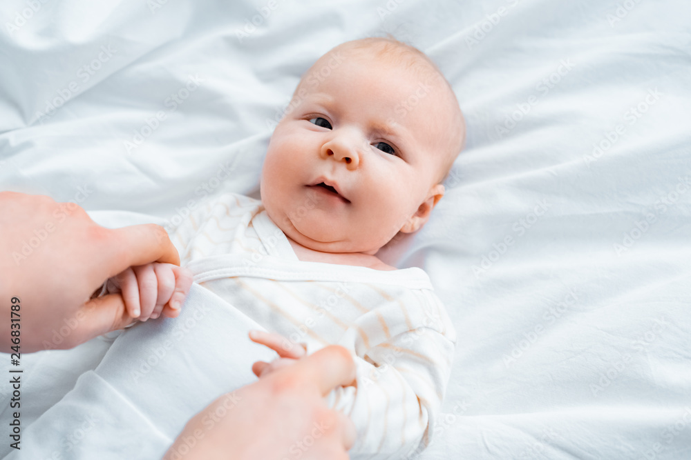 cropped shot of mother holding hands of adorable infant baby lying on white bedding cropped shot of mother holding hands of adorable infant baby lying on white bedding