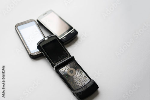 Three mobile phones of old models on white background. One of the phones is a clamshell. Selective focus. Copy space.