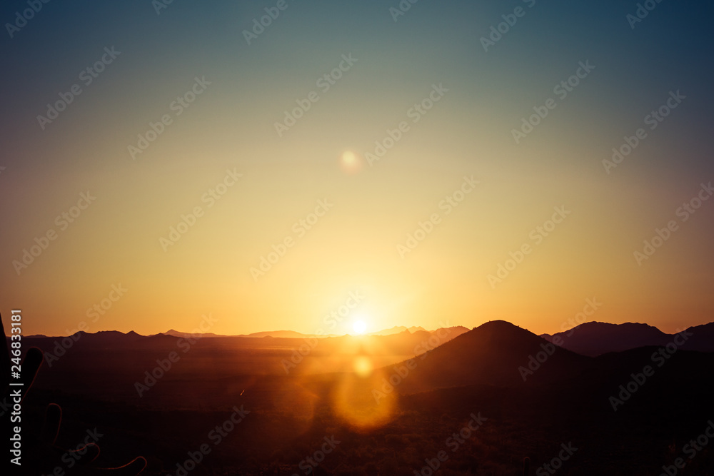 Obraz premium Słońce wschodzące nad pustynią w Arizonie z czterema szczytami w odległym tle i czystym błękitnym niebem.