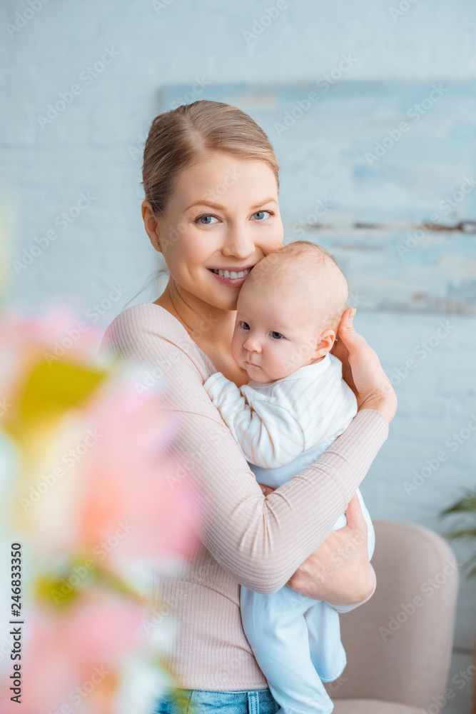 selective focus of happy young mother hugging adorable baby and smiling at camera - obrazy, fototapety, plakaty 