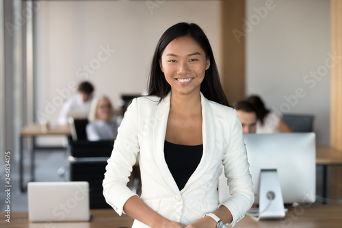 Smiling young asian business woman looking at camera, happy chinese employee worker, team leader, coach or corporate manager posing in office, millennial korean professional head shot portrait