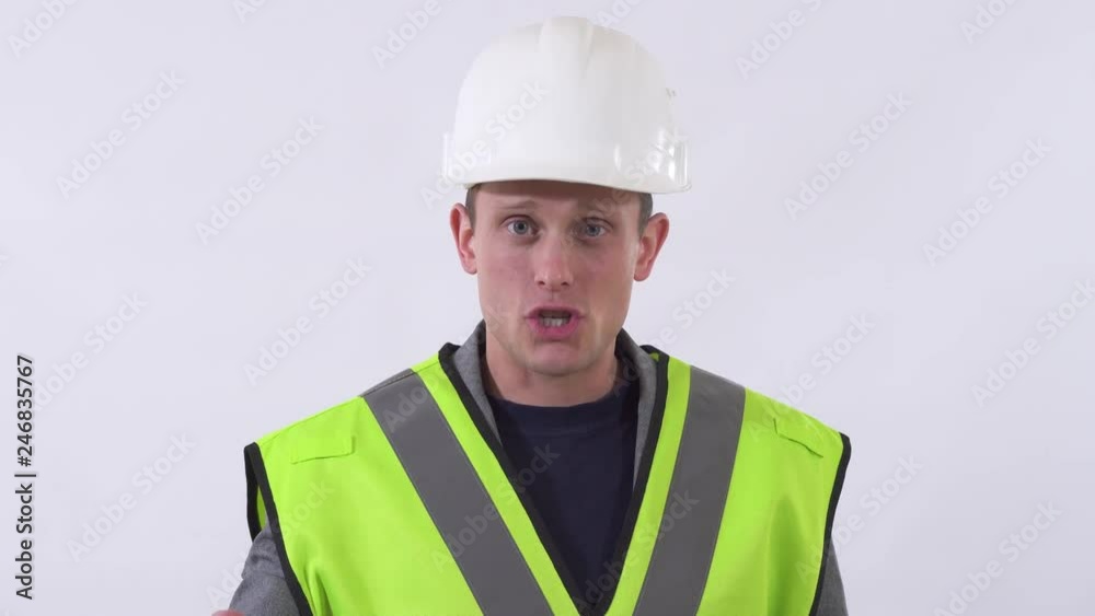 Portrait of a confident guy in a builder uniform and white helmet on his head talking to the camera giving advice and instructions. Shooting in the studio on a white background. Portrait of a confident guy in a builder uniform and white helmet on his head talking to the camera giving advice and instructions. Shooting in the studio on a white background.