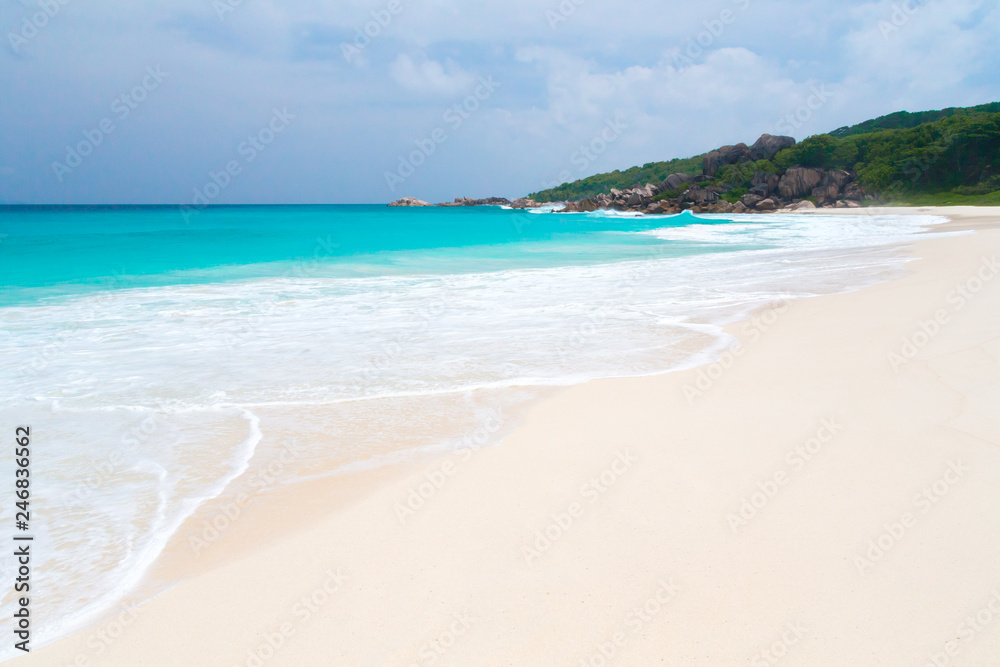 White sand beach with waves and hills with green plants