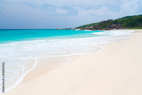 White sand beach with waves and hills with green plants