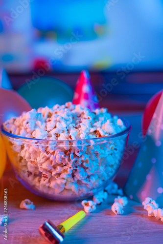 Popcorn with festive accessories on the background of TV. Watching TV on the occasion of a family celebration or in a circle of friends. Color and sevremenny light