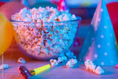 Popcorn with festive accessories on the background of TV. Watching TV on the occasion of a family celebration or in a circle of friends. Color and sevremenny light
