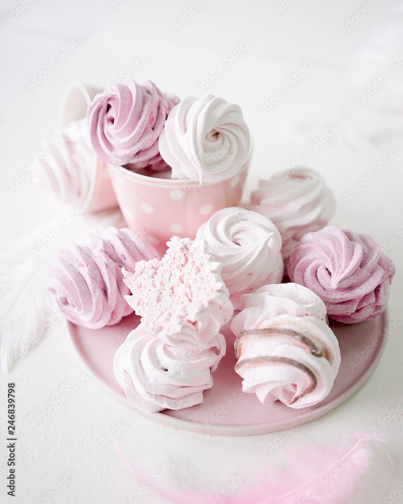 White and pink meringues on white background. Pink plate and cup on polka dot