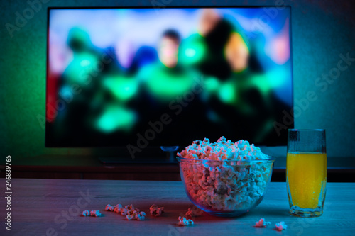 Popcorn in a glass plate with a drink on the background of the TV with the film on. Color bright lighting. Rest  relax  rest at home. Background