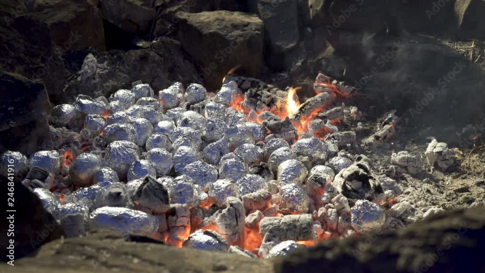 Campfire cooking Baked Potatoes. A camp fire with potatoes roasting in aluminium foil in the hot coals Campfire cooking Baked Potatoes. A camp fire with potatoes roasting in aluminium foil in the hot coals