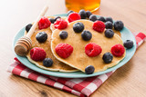Pancakes with raspberries, blueberries and honey on wooden table