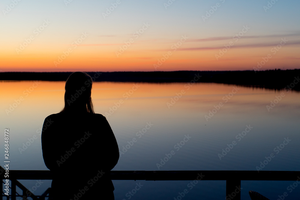 Fototapeta premium Young woman at sunset near lake silhouette