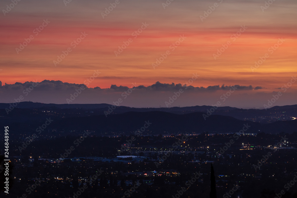 Suburban lights, mountains, clouds and layers of color below an orange sunset sky above.