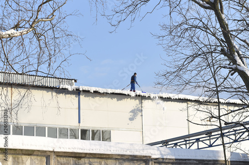 man removes snow from the roof of a building