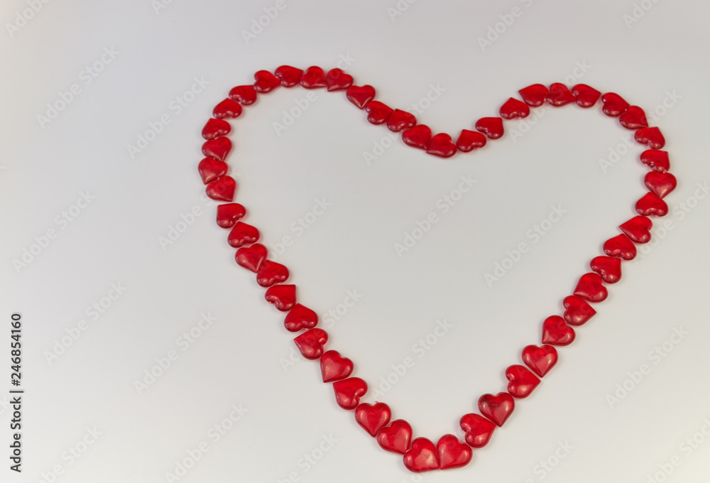 Heart-shaped laid out of small glass hearts on white background. Top view. Valentine's Day. Symbol of love. Copy space.