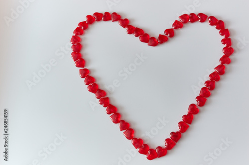 Heart-shaped laid out of small glass red hearts on white background. Top view. Valentine s Day. Symbol of love. Copy space.