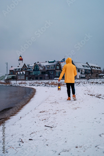 Men with yellow rain coat and oil lamp at the beach of Urk Netherlands during snowy winter weather, winter wonderland Lighthouse Urk Holland Netherlands photo