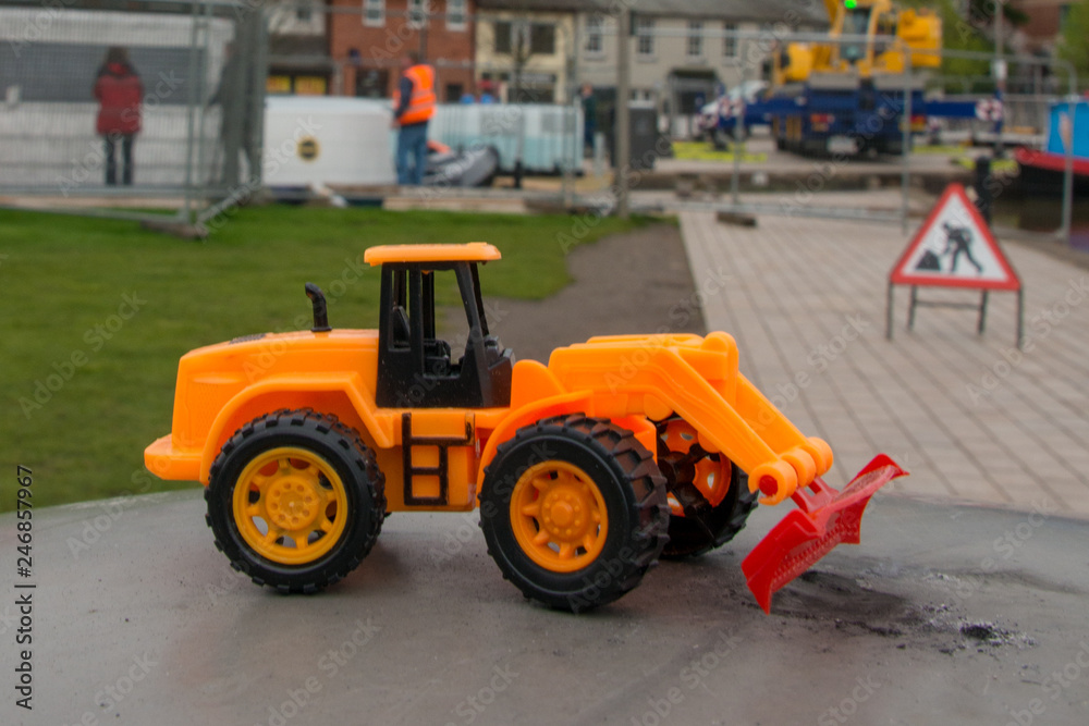 funny toy bulldozer with genuine building work and equipment in the background funny toy bulldozer with genuine building work and equipment in the background