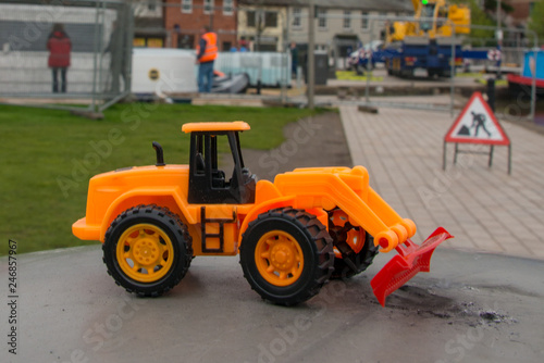 funny toy bulldozer with genuine building work and equipment in the background
