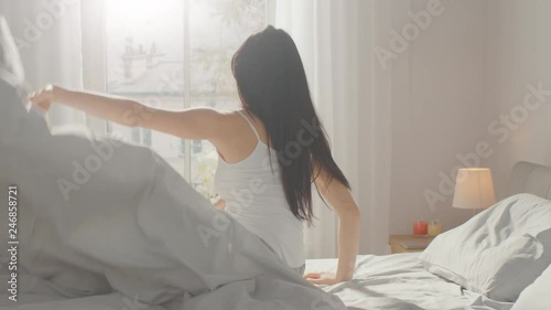 Beautiful Brunette Slowly Waking up in the Morning, Stretches and Gets Up from the Bed, Sun Shines on Her From the Big Window. Happy Young Girl Greets New Day.