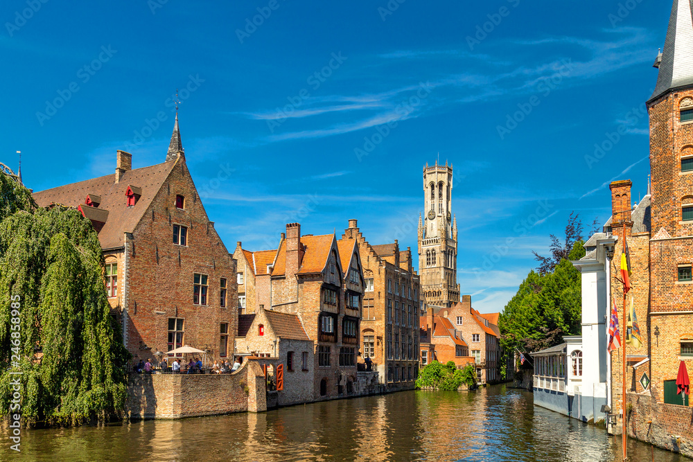 The Rozenhoedkaai canal in Bruges with the belfry in the background. Typical view of Bruges (Brugge), Belgium with red brick houses with triangle shaped roofs and canals.