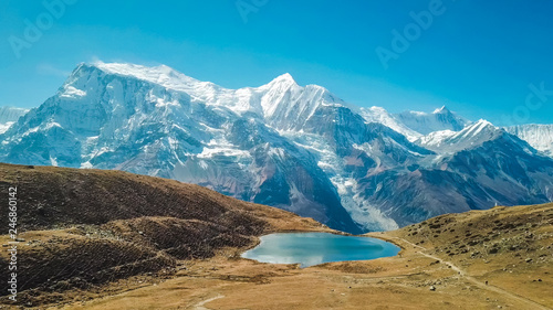 Ice lake, as part of the Annapurna Circuit Trek detour, Himalayas, Nepal. Annapurna chain in the back, covered with snow. Clear weather, dry grass, snowy peaks. Freedom, relax. High altitude lake.
