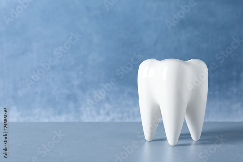 Ceramic model of tooth on table against color background. Space for text
