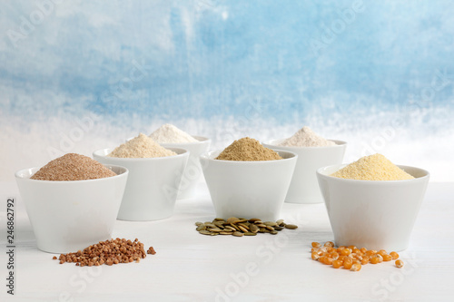 Bowls with different types of flour and seeds on table against color background. Space for text