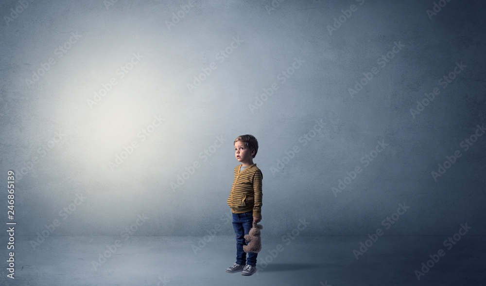 Little waggish kid staying alone in a big empty room with his plush
