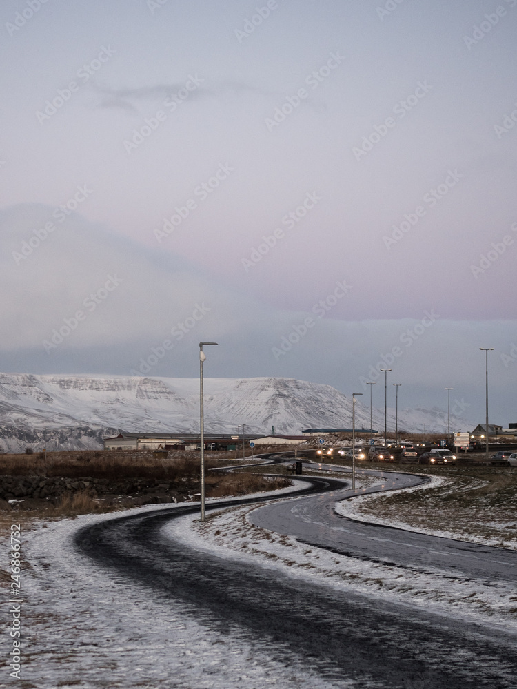 View on a street in the city of Reykjavik, Iceland. Photographed in the evening in winter, there is snow on the road. At the bottom we can see the tower of the city's cathedral.