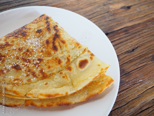 Traditional french crepe (or pancake) on a white plate, with sugar on top, dark brown wood background