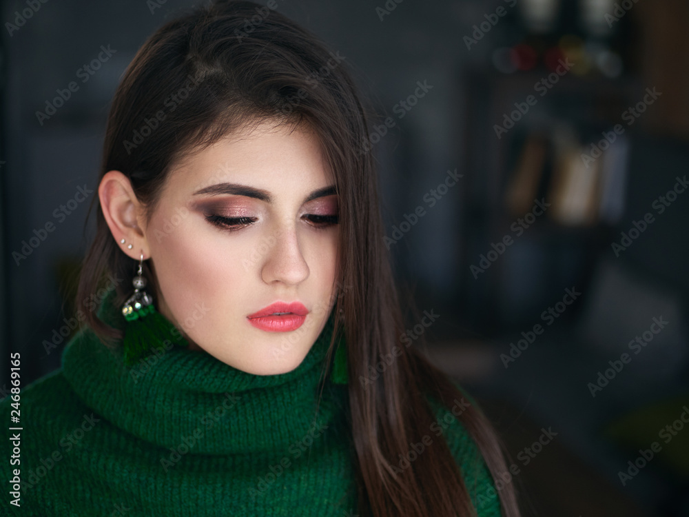 Fototapeta premium Dorywczo bliska portret szczęśliwa młoda brunetka kobieta modny makijaż zielony sweter i niestandardowe kolczyki pędzla.
