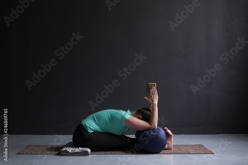 woman practicing yoga, Seated forward bend pose, using block and bolster photo