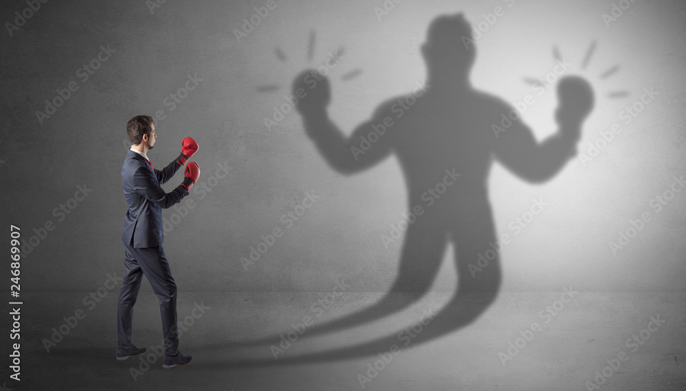 Fototapeta premium Businessman trying to fight with his unarmed shadow 