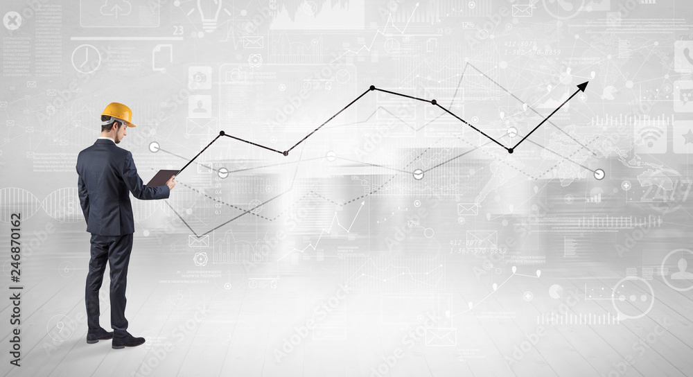 Engineer with construction helmet holding a plan and standing with graphs, charts and reports on the background Engineer with construction helmet holding a plan and standing with graphs, charts and reports on the background
