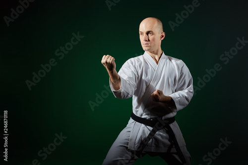 Adult athlete performs formal karate exercises on a dark green background