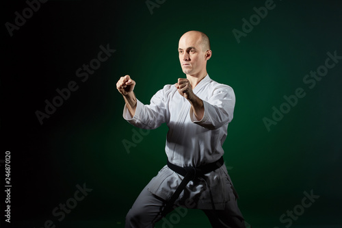 Adult athlete doing formal karate exercises on a dark green background