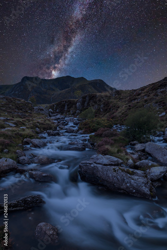 Digital composite Milky Way image of Moody landscape image of river flowing down mountain range near Llyn Ogwen and Llyn Idwal in Snowdonia