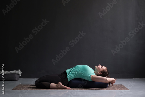 Beautiful athletic girl doing yoga supta virasana asana using bolster