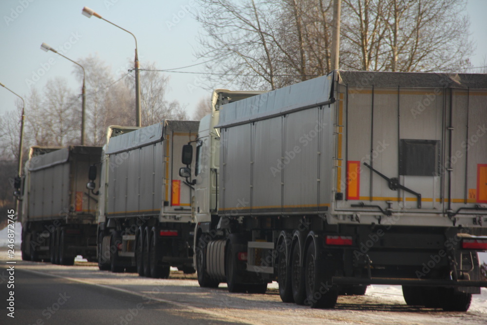 Three heavy trucks trucks with semi-trailers on roadside in winter day