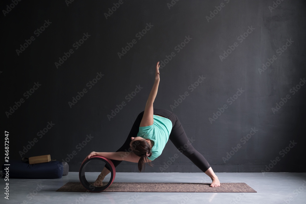 Woman doing yoga asana Wide Legged Forward Bend using special wheel. - obrazy, fototapety, plakaty 