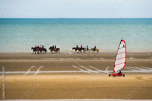 Plenty of horseback riders at the beach taking a ride with a sand yacht in the foreground